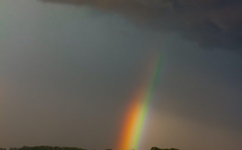 the end of a rainbow emerging from storm clouds over fields