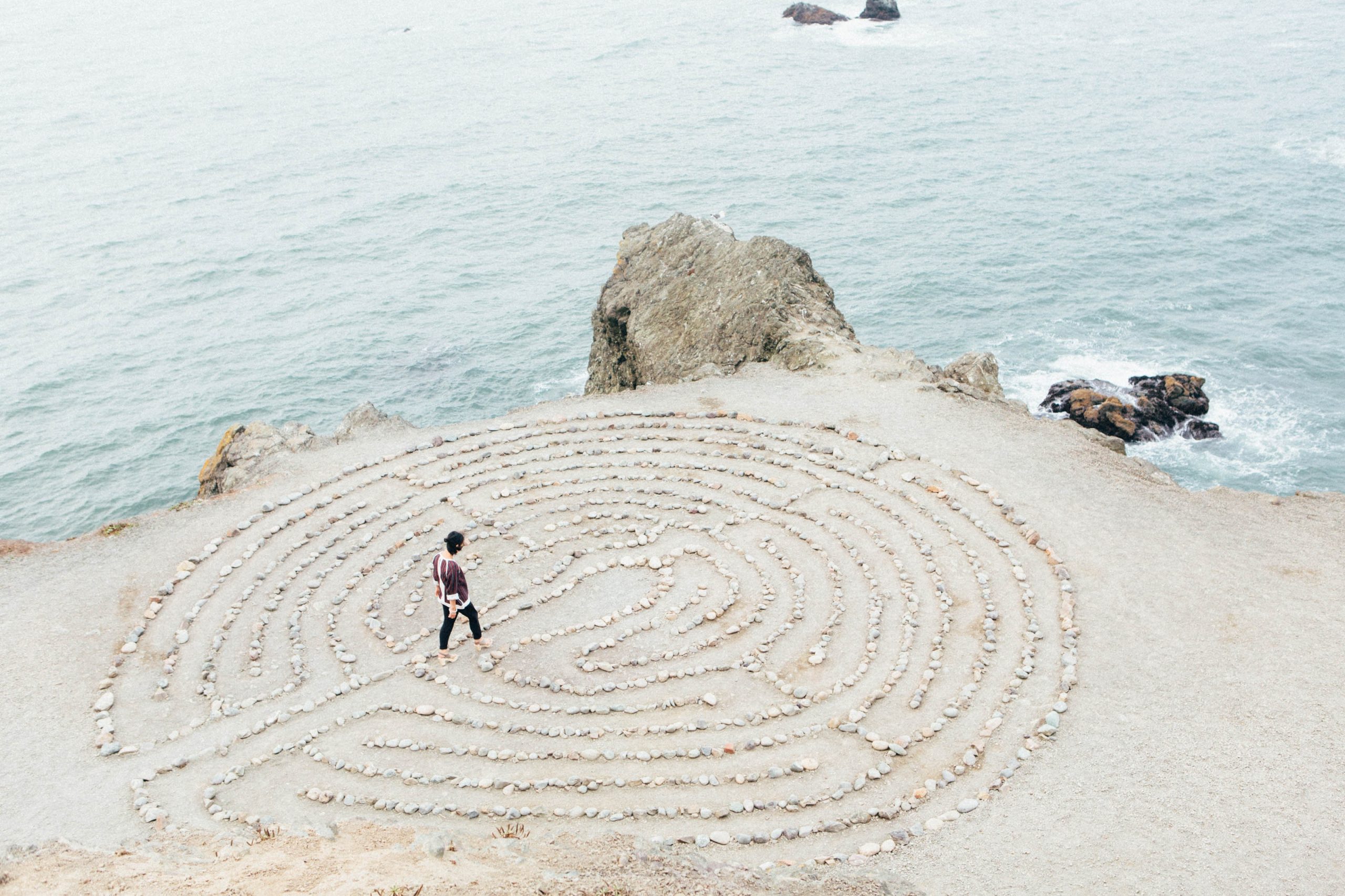 a person walks into a labyrnith drawn onto a pale sand beach