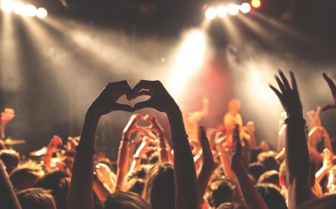 a person with two arms raised in a crowd, making a heart shape with both hands