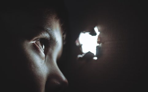 a child looks through a small hole from within a cardboard box. light comes through the hole in the box.