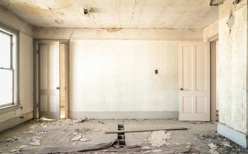 interior photo of a room that is old and beginning to fall apart. the paint and wallpaper are peeling and there are broken wooden slats in the floor.