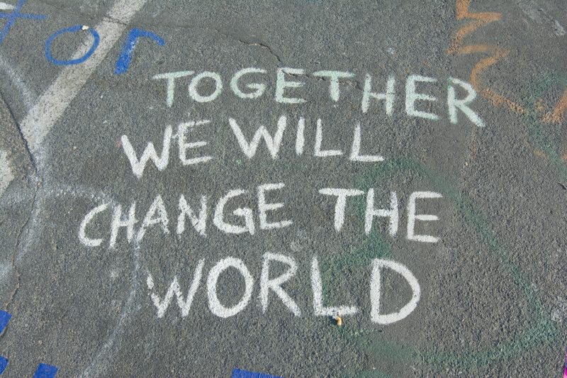 written in white chalk on pavement are the words 'TOGETHER WE WILL CHANGE THE WORLD'