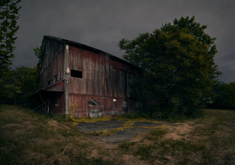 an old barn with fading red paint beside a large tree, against a midwest summer stormcloud background