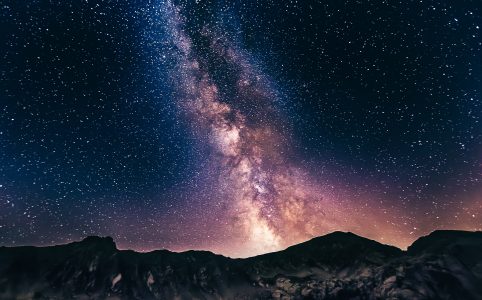 an intense photo of the milky way across a starry siky. mountains are silhouetted against the sky in the lower third of the photo.