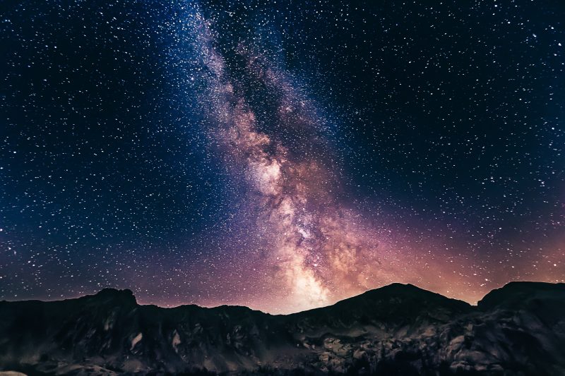 an intense photo of the milky way across a starry siky. mountains are silhouetted against the sky in the lower third of the photo.