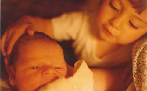 a warmly saturated photo of an infant on the left being gently touched on the head by a toddler (me) on the right.