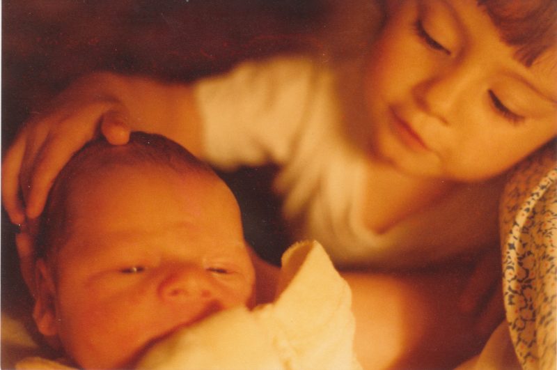 a warmly saturated photo of an infant on the left being gently touched on the head by a toddler (me) on the right.