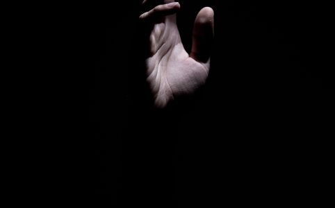 a hand reaching upward, lit from the right on an open palm, against a dark background