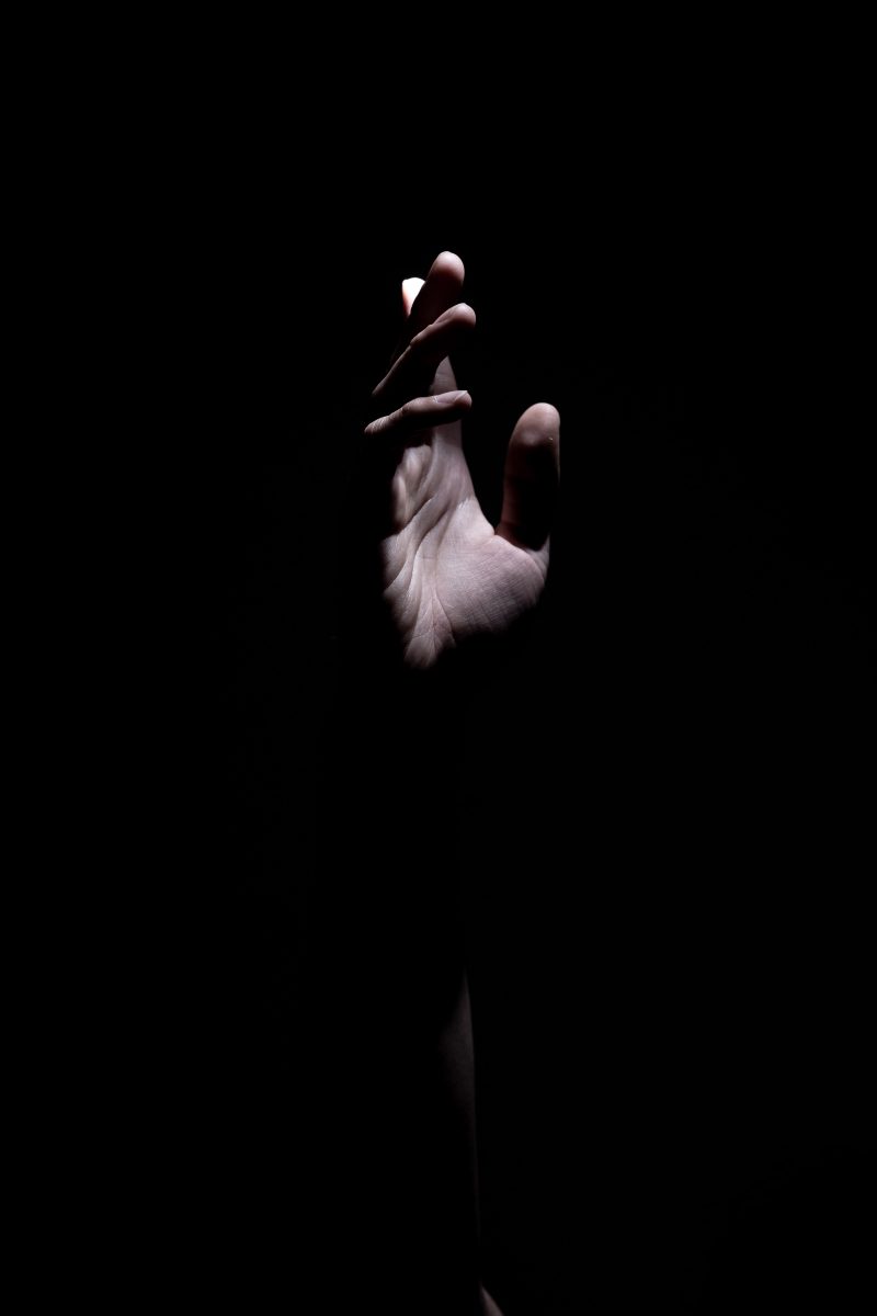 a hand reaching upward, lit from the right on an open palm, against a dark background