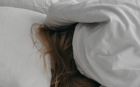a person underneath white blankets with white pillows, with only light brown hair showing beneath the covers