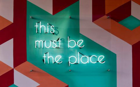 an orange, white, red, and turquoise wall with a neon sign with the words 'this must be the place'