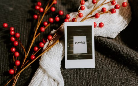 a photo of the word 'memories', framed in white, lying with a spray of red berries and a white cloth on a dark knit blanket