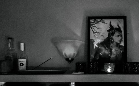 a black and white photo of my Loki shrine, a shelf with candles, incense, and a large framed likeness of the god Loki