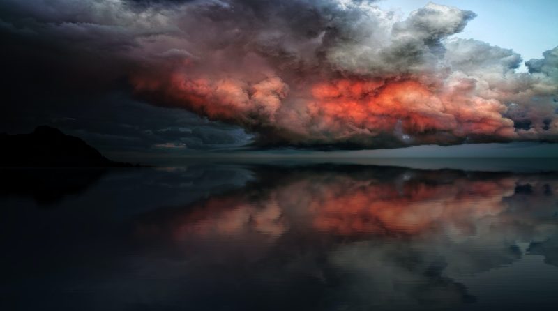 grey, black, and red lit clouds over a reflective lake surface